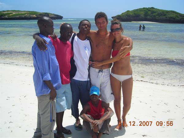 Group of friends hugging on white sand beach, green islands in background
