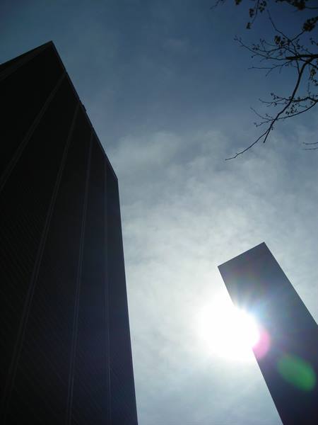 Dark skyscrapers against cloudy sky, sun rising between two towers