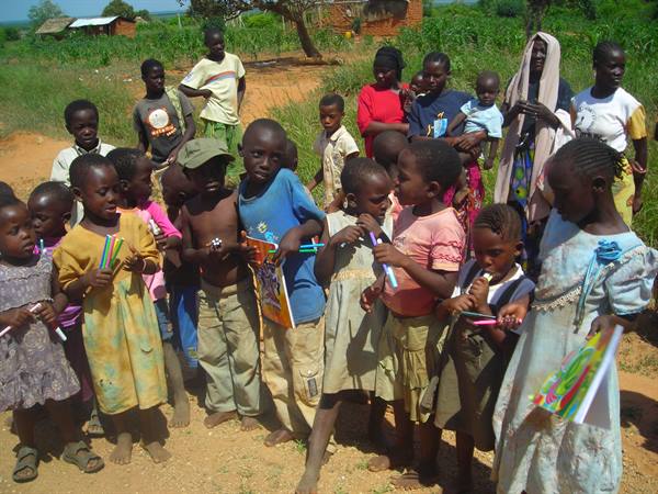 Children on African dirt road receiving markers and notebooks