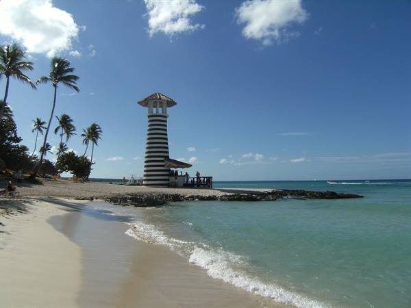 Black and white striped lighthouse on tropical beach with palms and turquoise sea