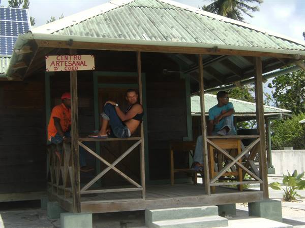 Three young men on the wooden porch of Centro Artesanal, green roof, solar panels