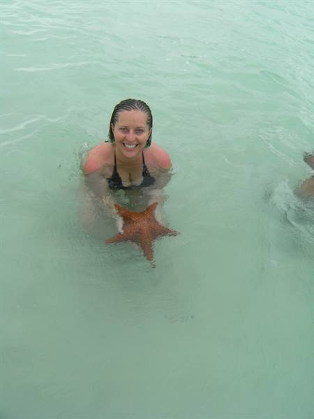 Smiling woman in black bikini holds an orange starfish in turquoise water