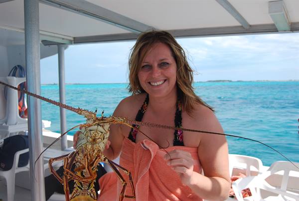 Smiling woman on a boat holding a large spiny lobster by turquoise water