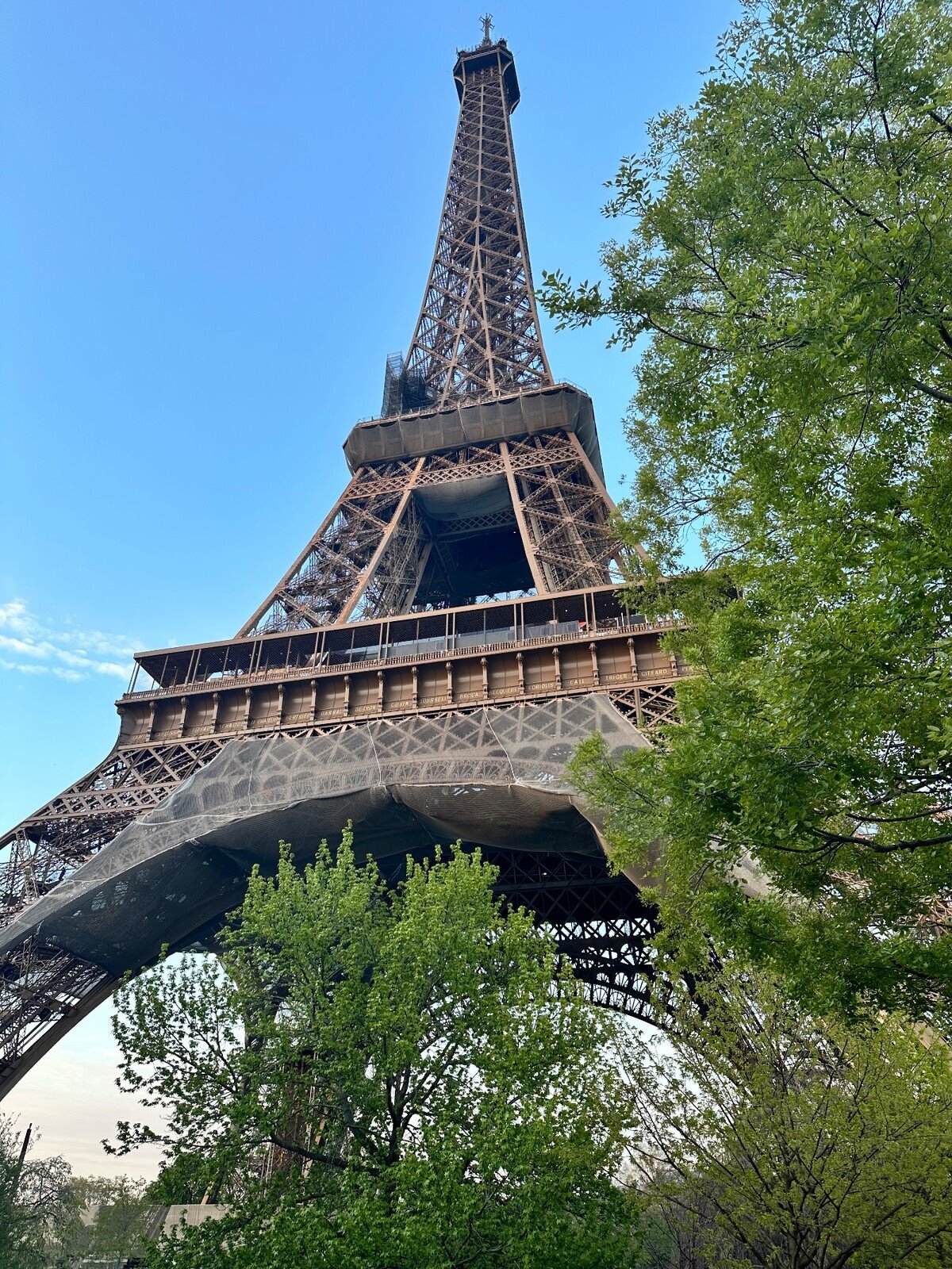La Tour Eiffel in ferro battuto vista dal basso tra alberi verdi e cielo azzurro
