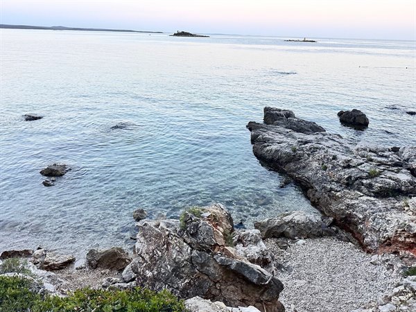 A quiet sunset over the crystal-clear sea among the rocks, a suspended moment.