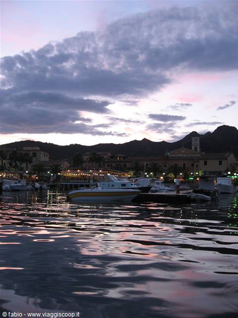 Boats moored at the harbor among lights and pink dusk clouds