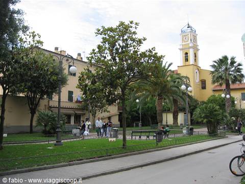 Garden with palm trees and yellow bell tower, people strolling along tree-lined path
