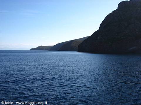 Dark cliffs plunging into blue sea, rocky coastline under clear sky