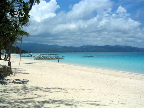 Traditional Filipino boats on white sand, turquoise sea, palms and mountains under clouds