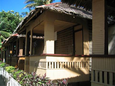 Wooden bungalows with thatched roofs and verandas, palms behind