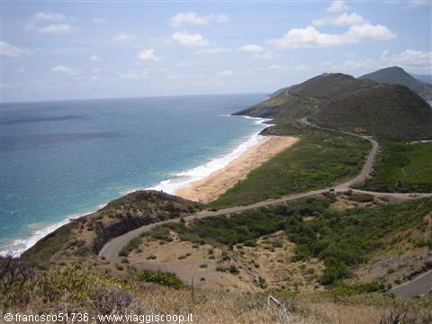 Golden sand beach below green hills, winding coastal road by turquoise sea in Saint Kitts