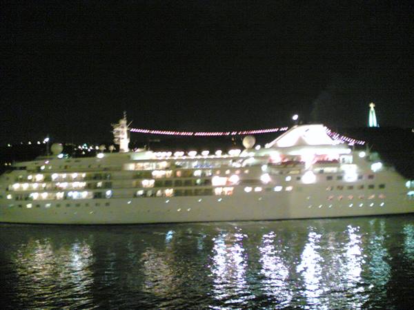 Illuminated cruise ship at night, lights reflecting on harbor water