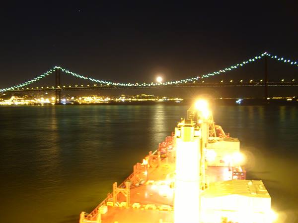 Illuminated suspension bridge at night seen from a cargo ship bow