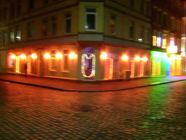 Night corner building with colorful lights, wet cobblestones, blurred motion