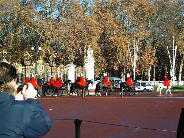 Mounted guards in red uniforms ride past the gilded gates of Horse Guards