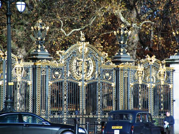 Ornate black and gold wrought iron gate with cars and autumn trees behind