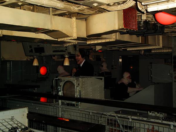 Visitors inside a warship's command bridge lit by red lights
