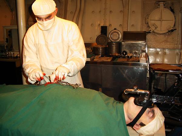 Surgeon in white gown operating on anesthetized patient in a submarine's operating room