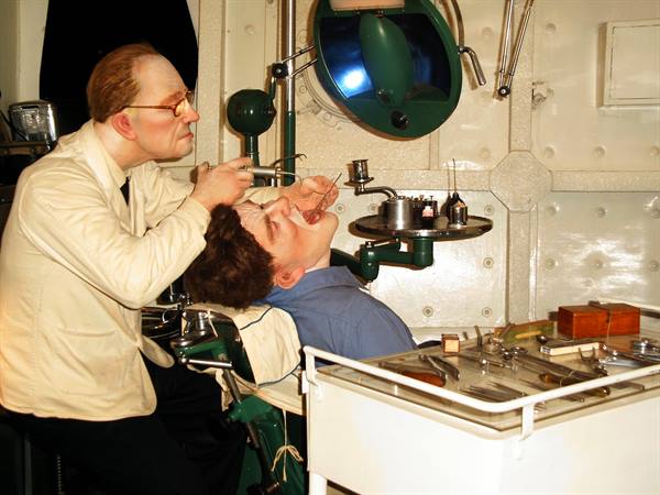 Wax figures: vintage dentist treating patient under lamp in museum display