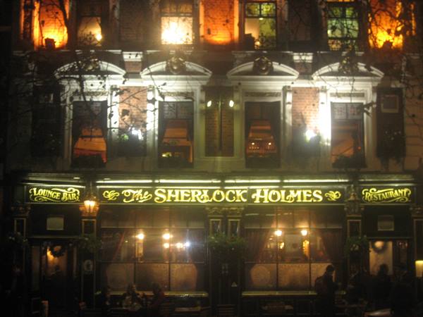 Golden sign of the Sherlock Holmes pub glowing at night, man walking past