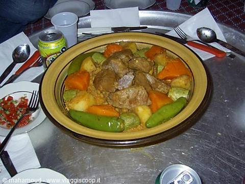 Couscous with meat and vegetables in traditional dish, cutlery and soda can on table