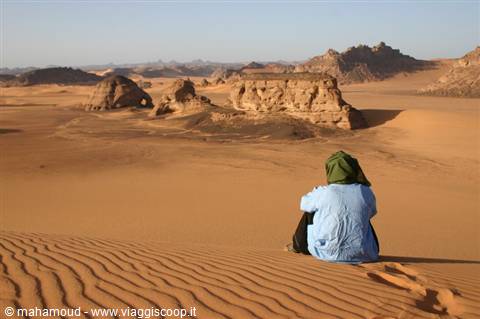 Man in green turban sitting on sand dune facing wind-carved rock formations