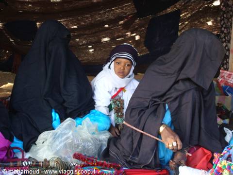 Black-veiled women and a child selling colorful goods at a shaded market