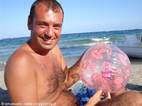 Smiling man on beach holding inflated pink ball, sea waves and white boat