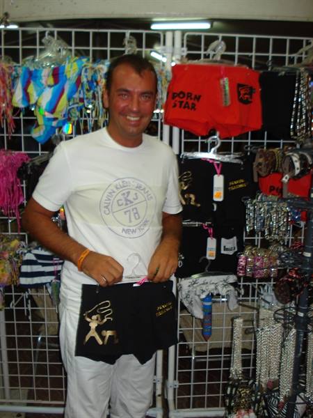 Smiling man in white t-shirt holds black boxer shorts at a market stall