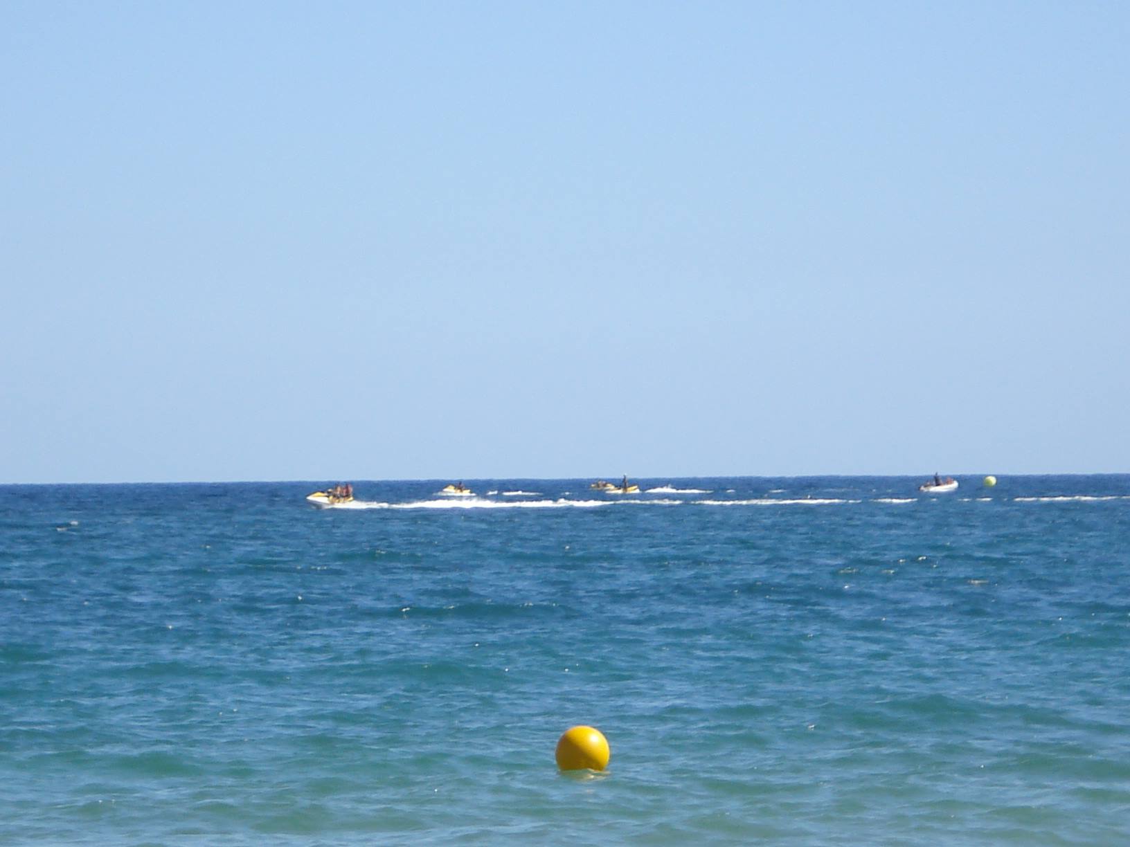 Jet skis and boats speed across blue sea, yellow buoy in foreground
