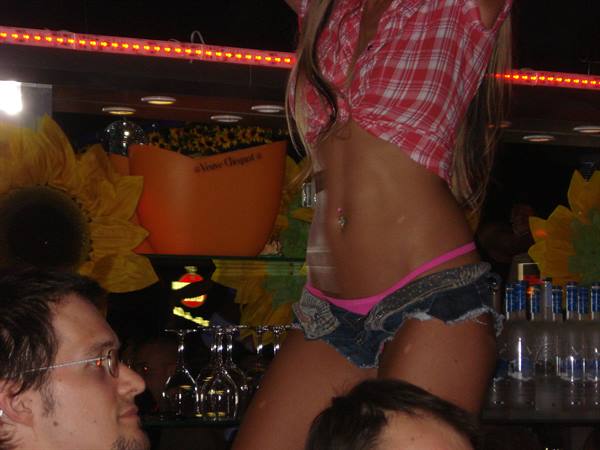 Girl in red plaid shirt dances on the bar counter among bottles