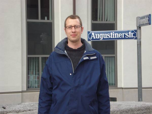 Man in blue jacket and glasses next to the Augustinerstr. sign