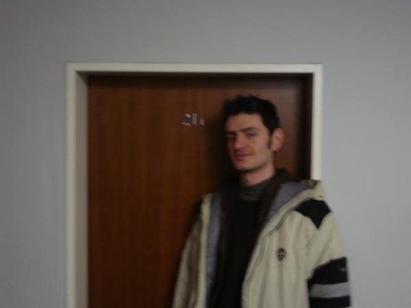 Young man in cream jacket standing by a wooden door, blurry shot