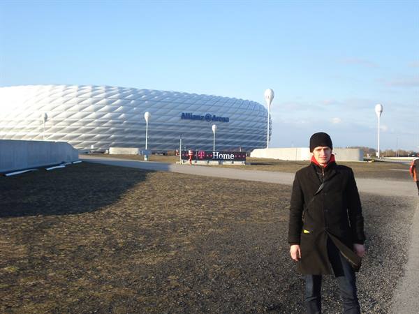 Young man in black coat in front of Munich's Allianz Arena