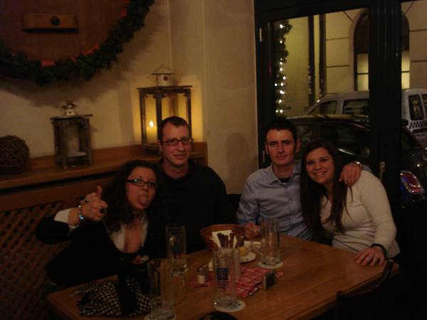 Four smiling friends at a wooden pub table, lit lanterns glowing