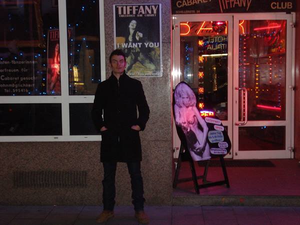 Man in black coat outside the Tiffany cabaret, red neon signs glowing
