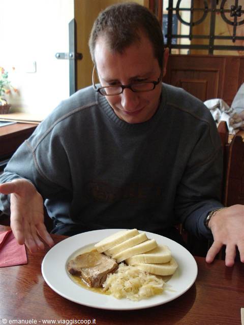 Man with glasses at restaurant facing plate of sauerkraut, meat and dumplings