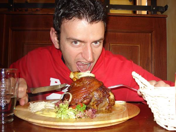 Man in red hoodie pretends to bite a huge pork knuckle in a tavern