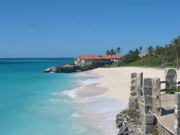 White sand beach with red-roofed houses, palm trees and old stone walls