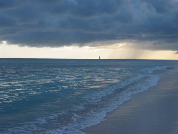 Sailboat under dark clouds, foamy waves washing the pale sandy shore