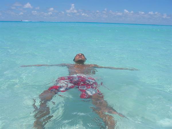 Man floats on his back in shallow turquoise water, red swim trunks