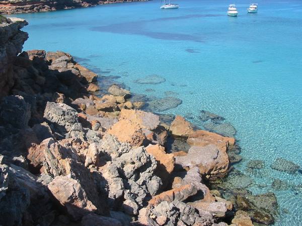 Red rocks by turquoise water, boats anchored in a sunny cove