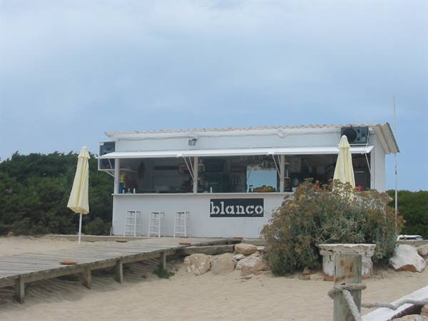 White beach kiosk labeled blanco, closed umbrellas, wooden boardwalk on sand
