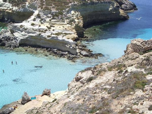 Turquoise water between white limestone cliffs, swimmers at Lampedusa, Rabbit Island