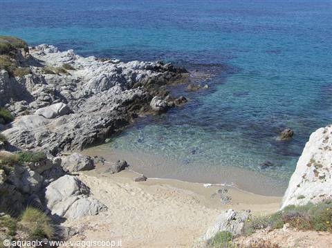 Small sandy cove between granite rocks, turquoise sea and clear water