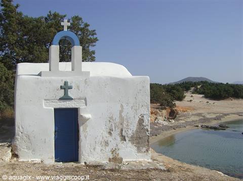 Small whitewashed chapel with blue door and bell tower by the sandy beach