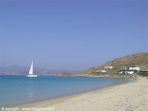 White sailboat on turquoise sea by sandy beach and dry hill
