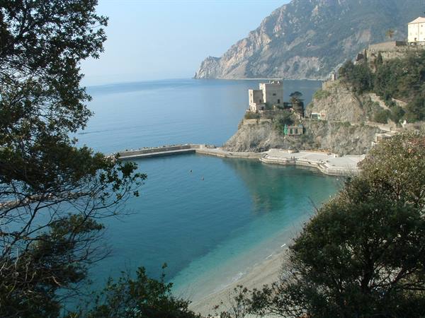 Old tower on the cliff above turquoise sea and beach in Monterosso al Mare