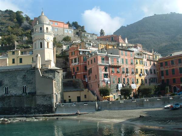 Colorful houses by the sea in Vernazza, bell tower and beach under cloudy sky