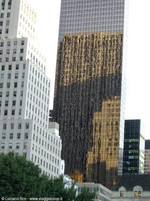 Golden reflective skyscraper tower between white buildings and trees in Manhattan